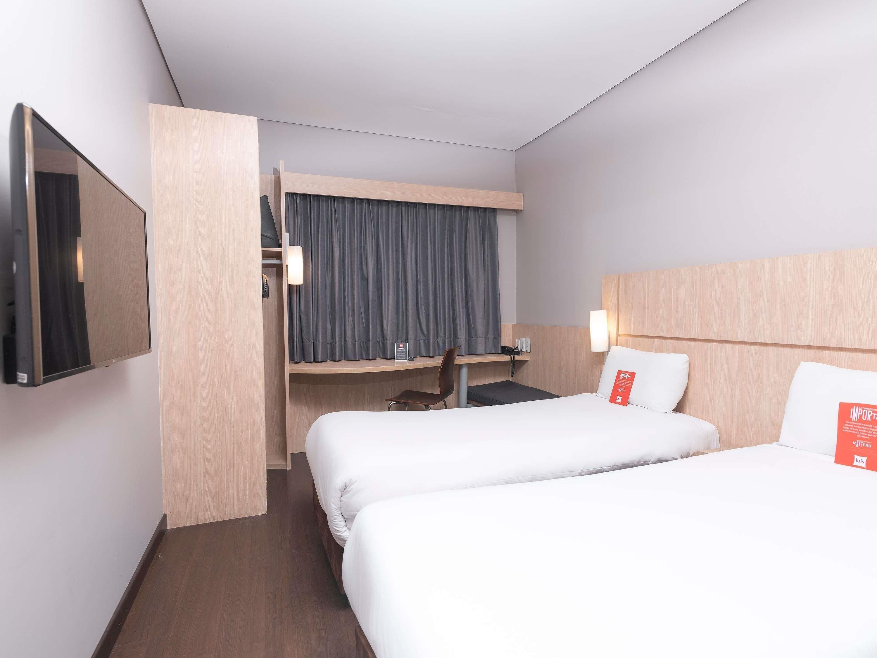 A hotel room with two beds, a desk, a chair, a TV, and a curtain.