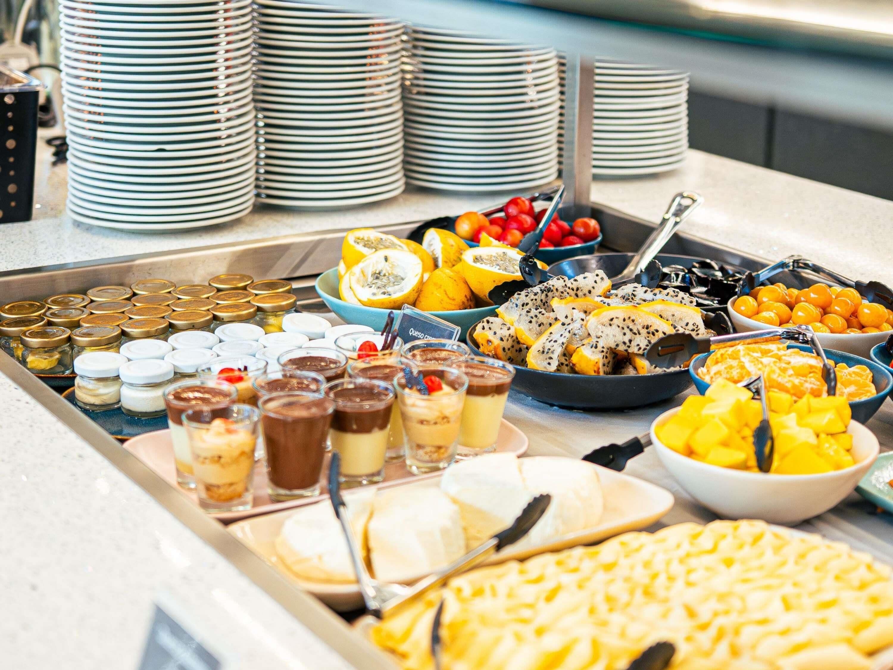 Un bufé con diversas opciones de comida, incluyendo frutas, postres y salsas.