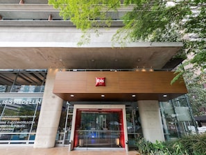 En hotellentrén med modern design, en tydlig skylt med texten ”ibis Hotels”, och en glasfasad som speglar omgivningen.
