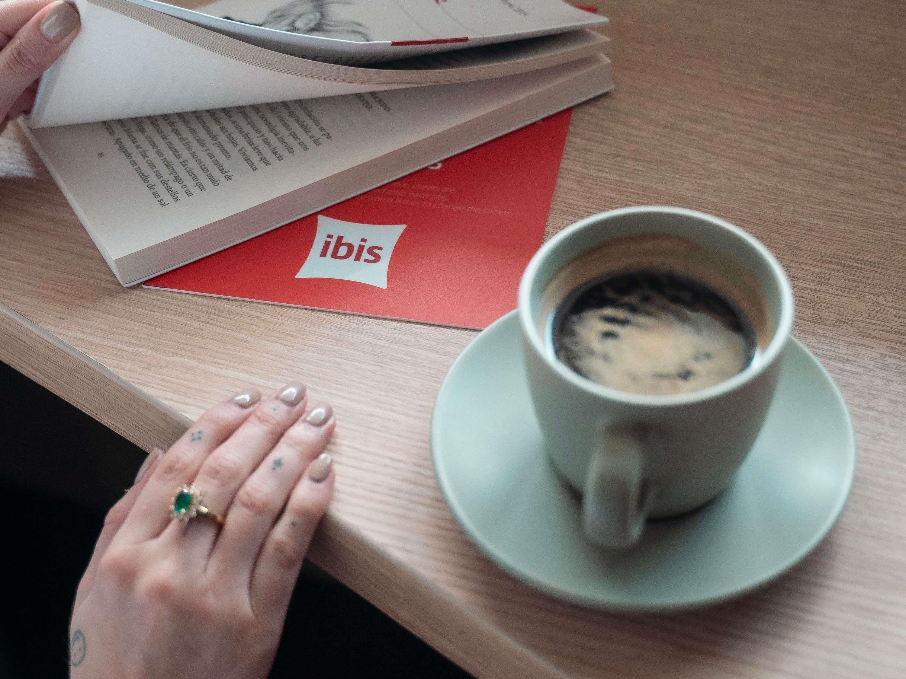 Una mano descansando sobre una mesa con una taza de café y un libro.