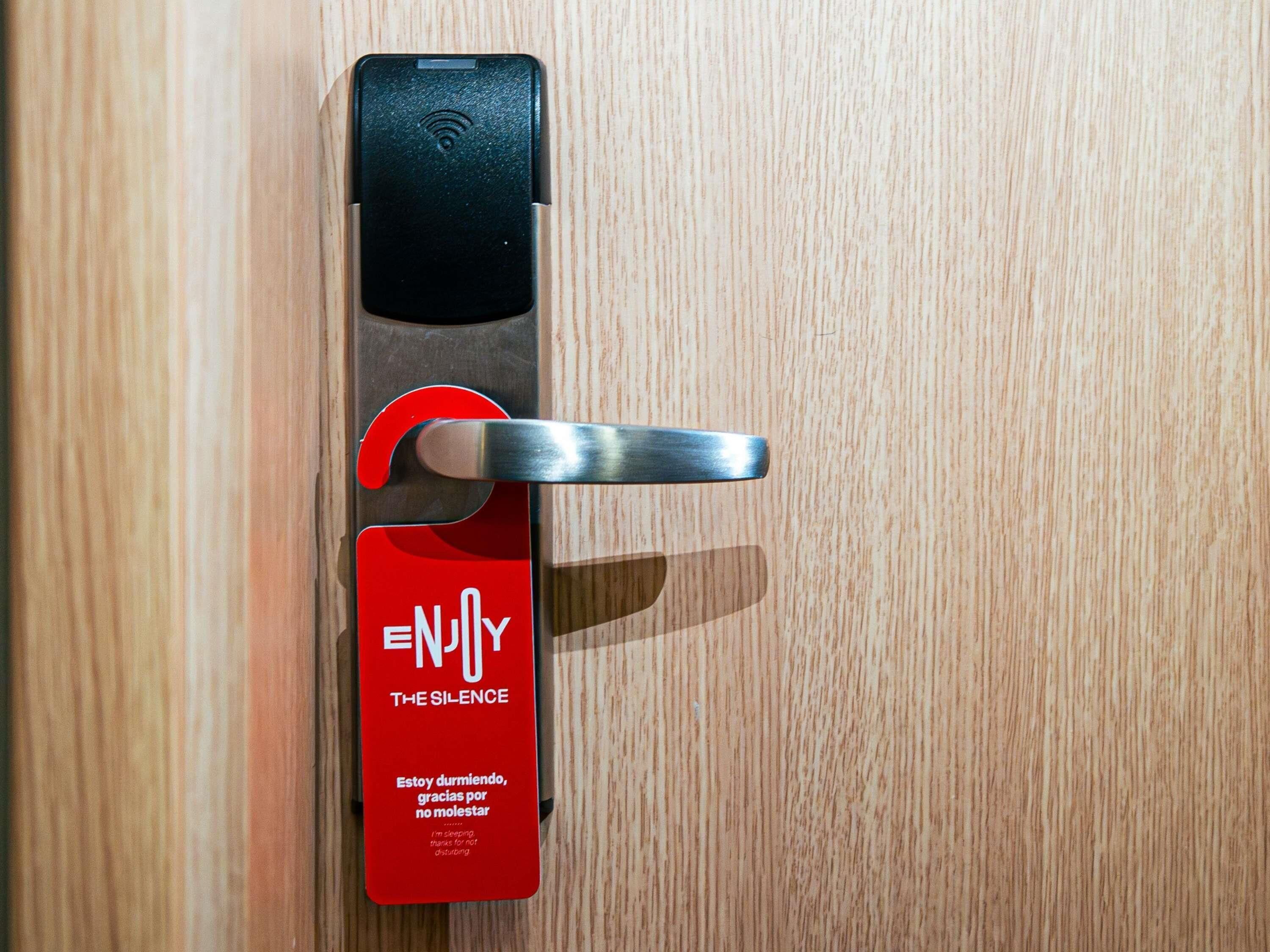 A door with a keycard reader and a red card labeled "ENJOY THE SILENCE" with a message in Spanish.