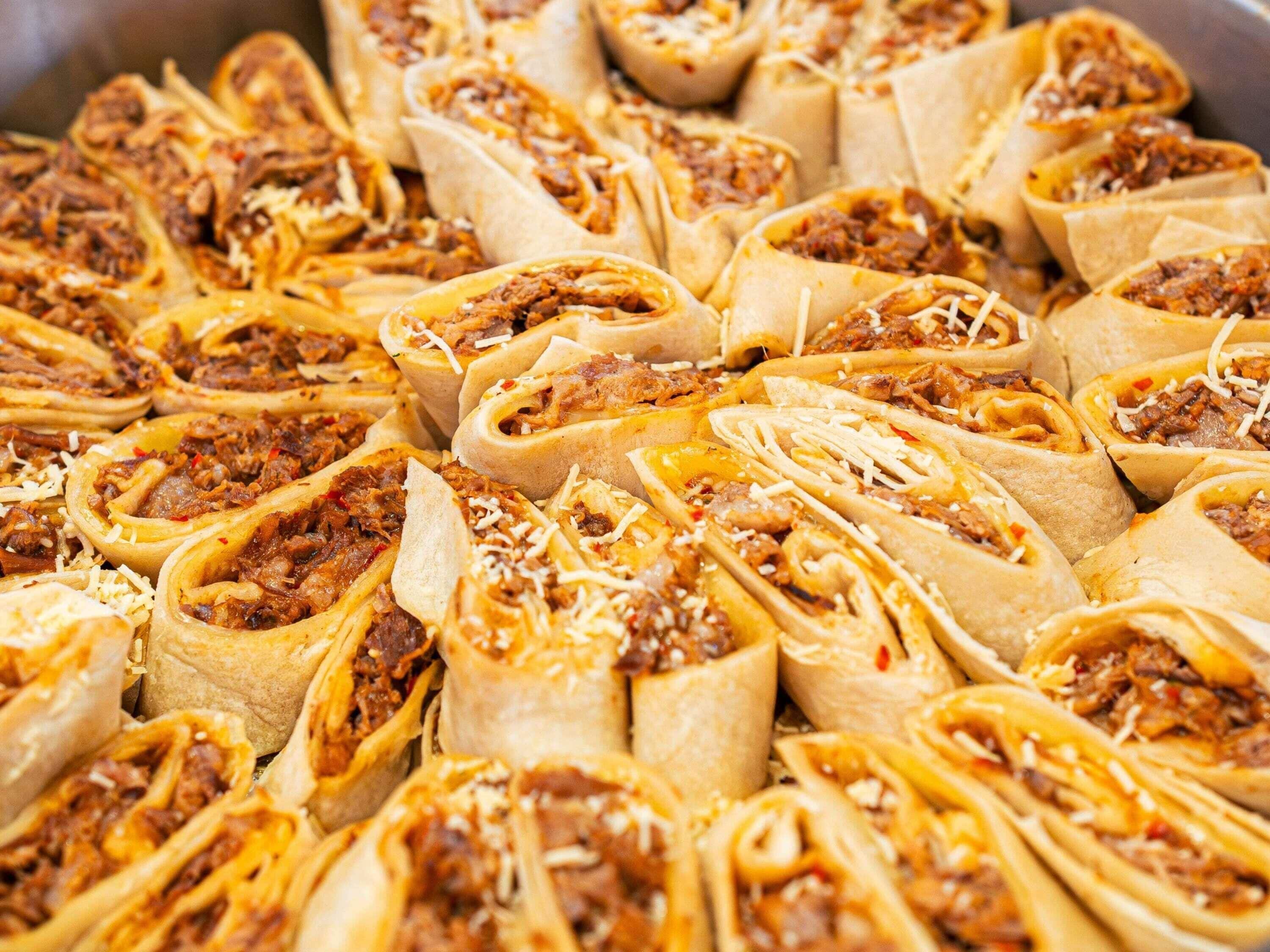A tray of burritos with meat and cheese.