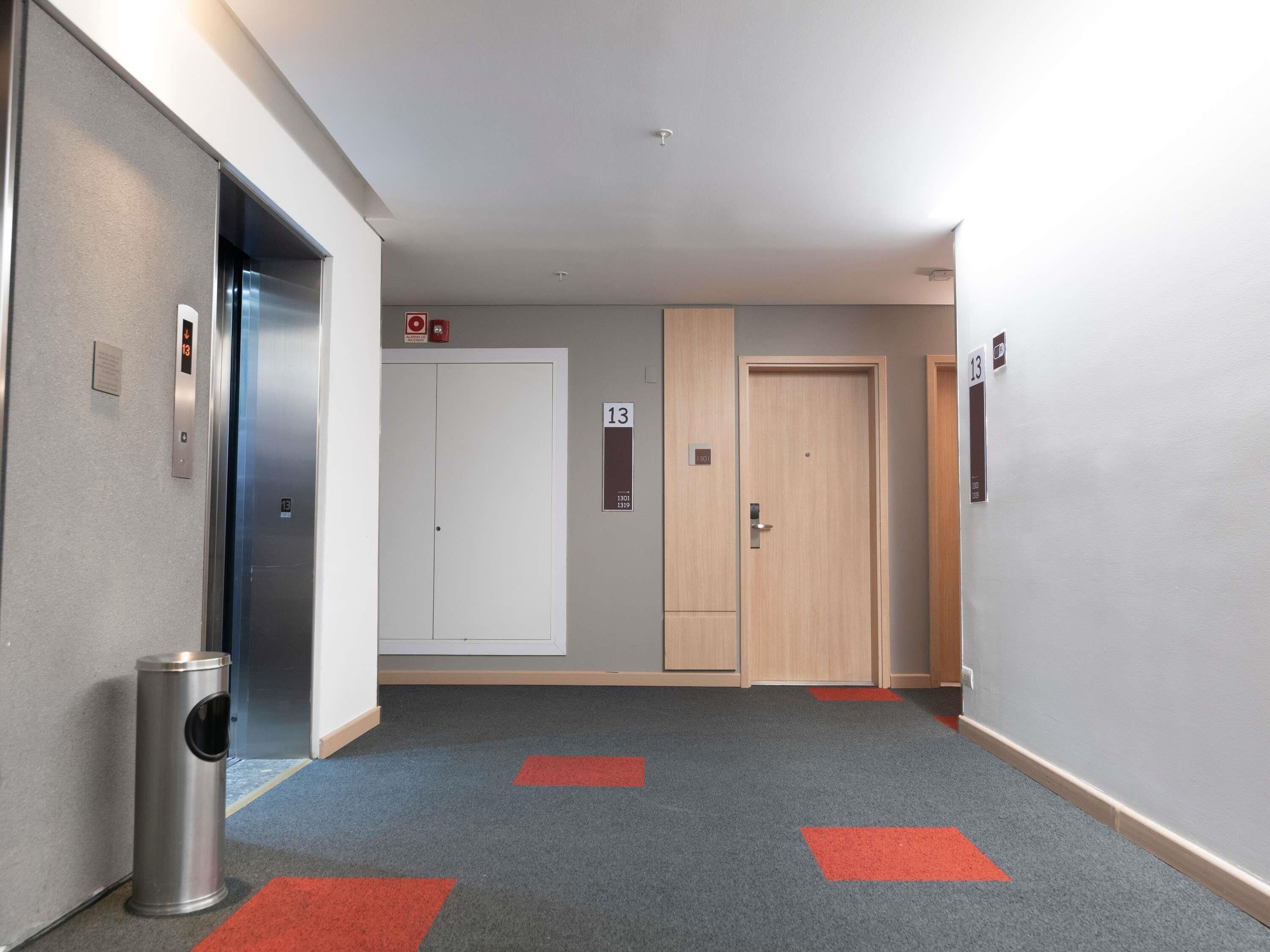 A hallway with an elevator, a trash bin, and doors numbered 13 and 1301.