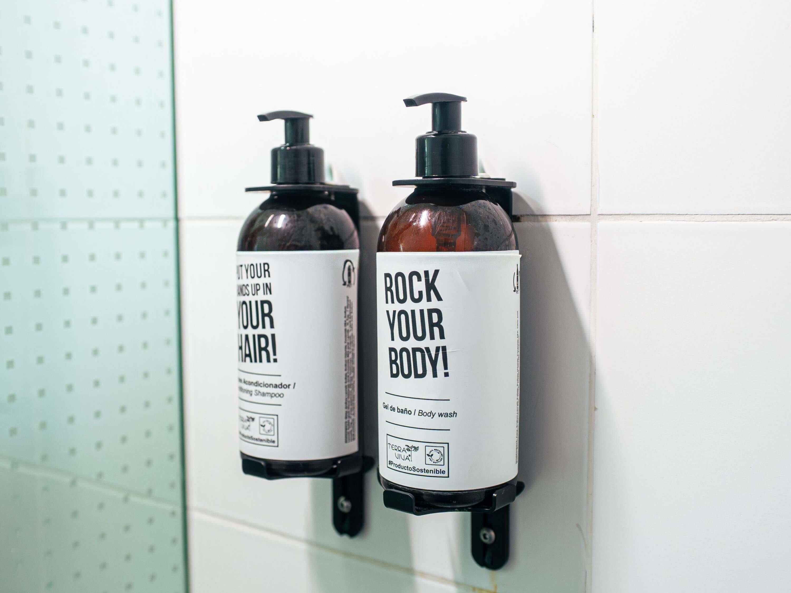 Dos dispensadores montados en la pared, uno para acondicionador y otro para jabón de cuerpo.