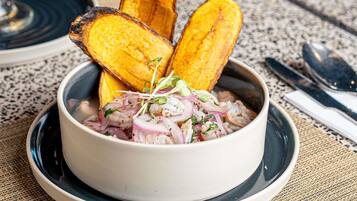 A bowl of shrimp cocktail with red onions and herbs, accompanied by grilled plantain slices on a plate.