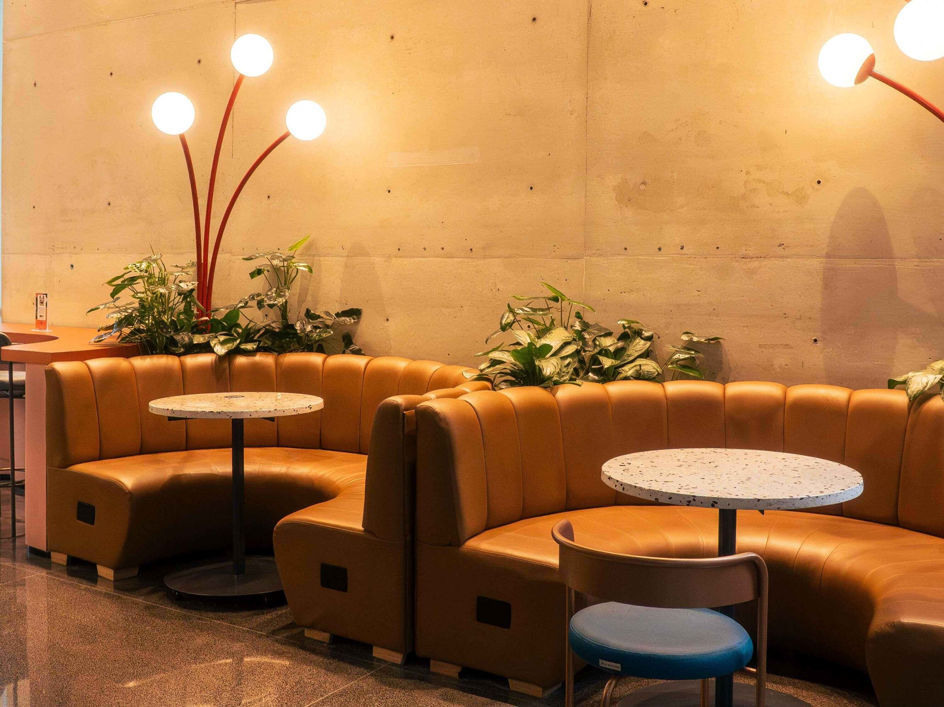 A modern lounge area with leather seating, round tables, and potted plants.