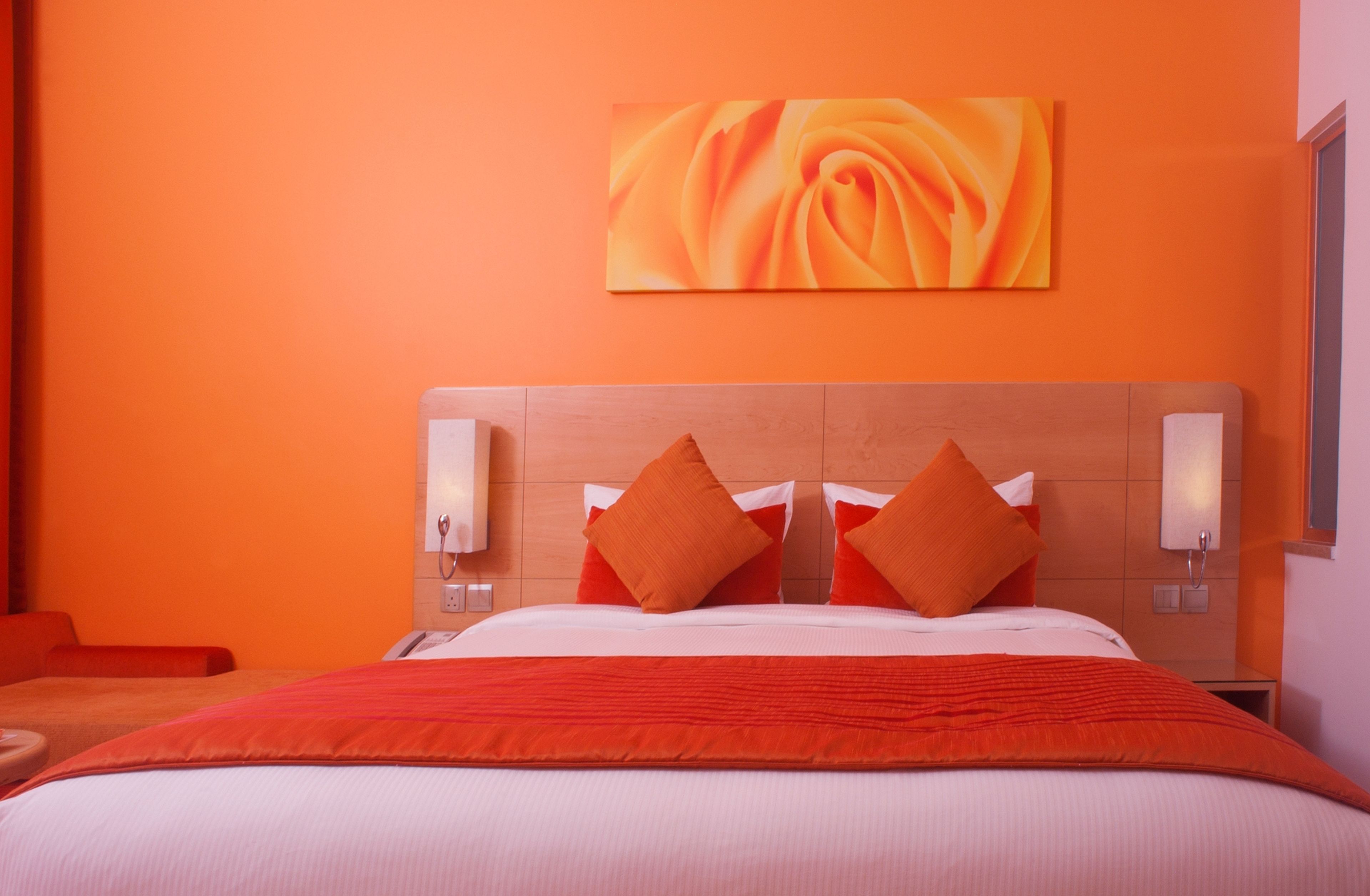 A hotel room with a large bed, orange walls, and a painting of a rose.