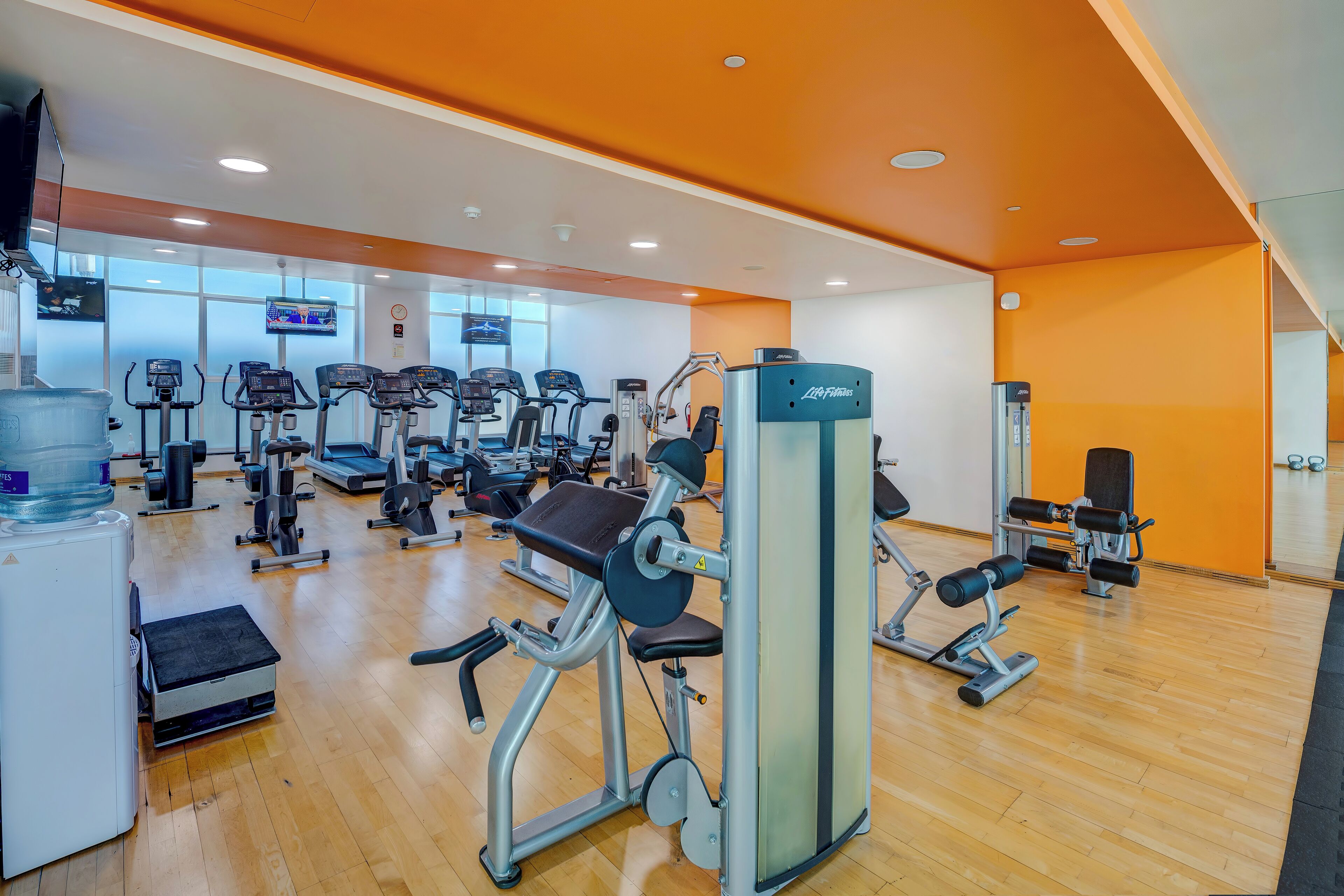 A gym with various exercise machines, a water dispenser, and a large mirror.