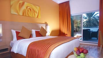 Ein Hotelzimmer mit einem großen Bett, einer Glastür, die auf einen Balkon führt, und einer Obstschale auf einem Nachttisch.