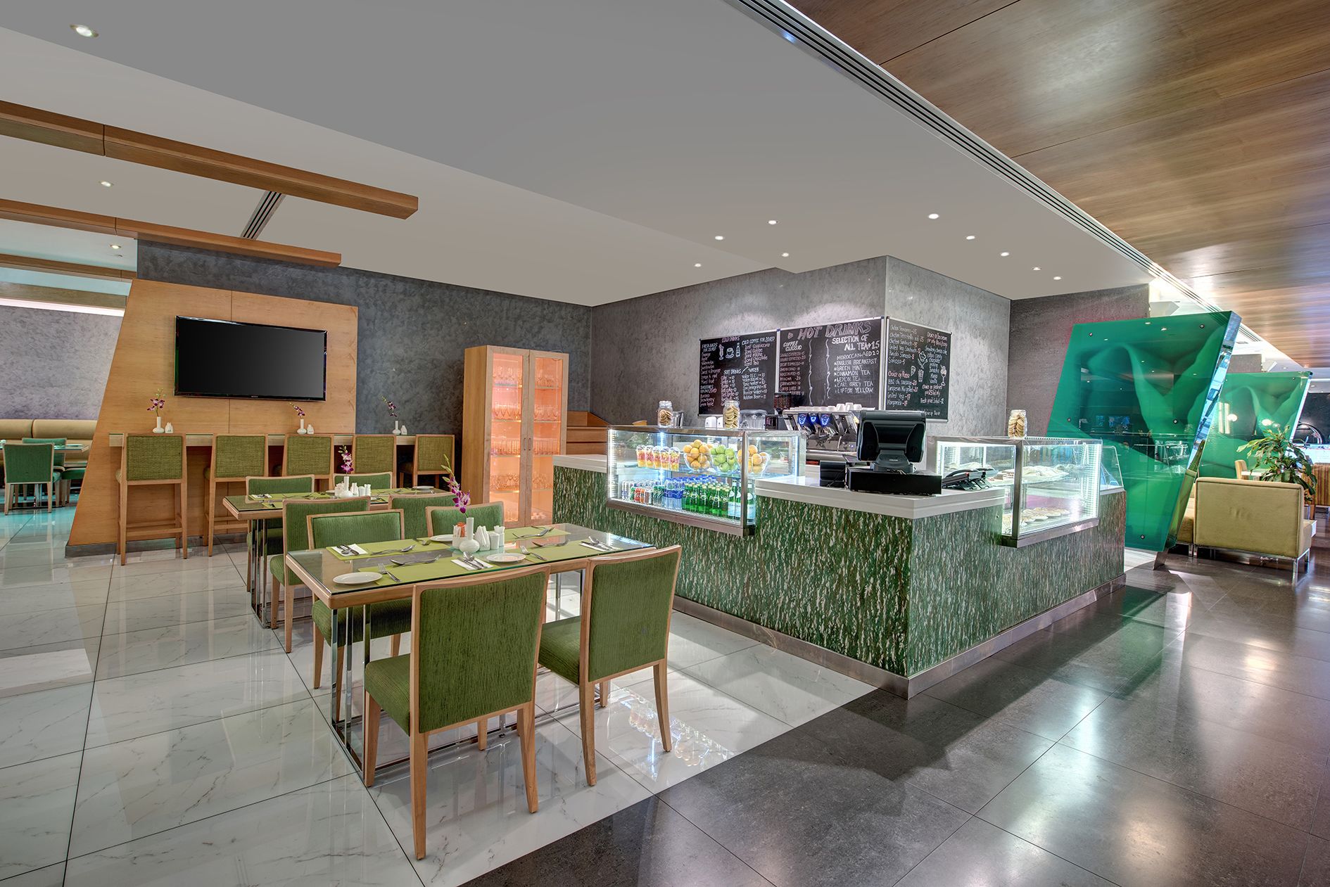 Un restaurant moderne avec un comptoir central, des chaises à l’assise rembourrée de tissu vert et un tableau affichant le menu.