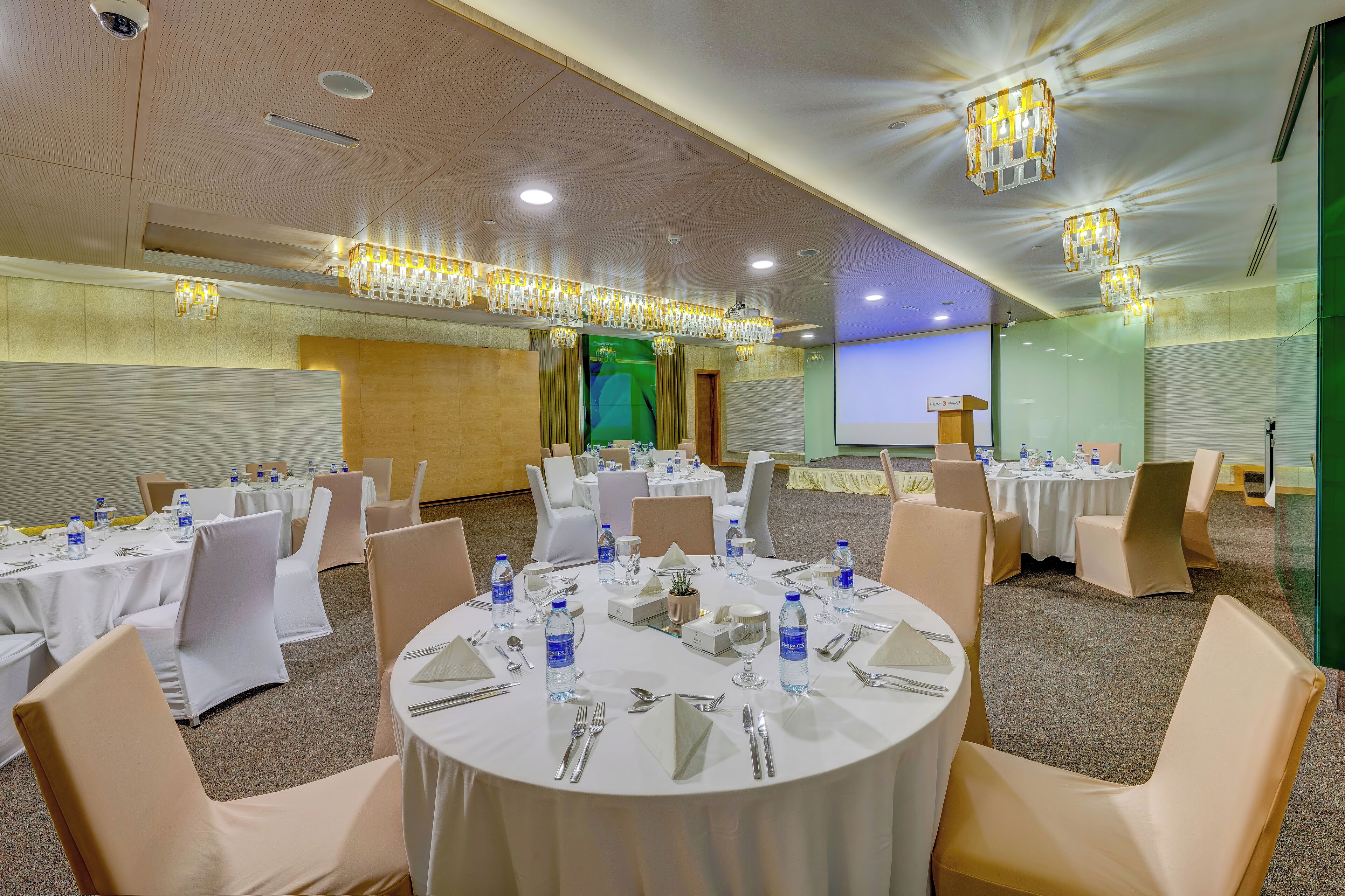 A conference room with round tables, white tablecloths, and beige chairs.