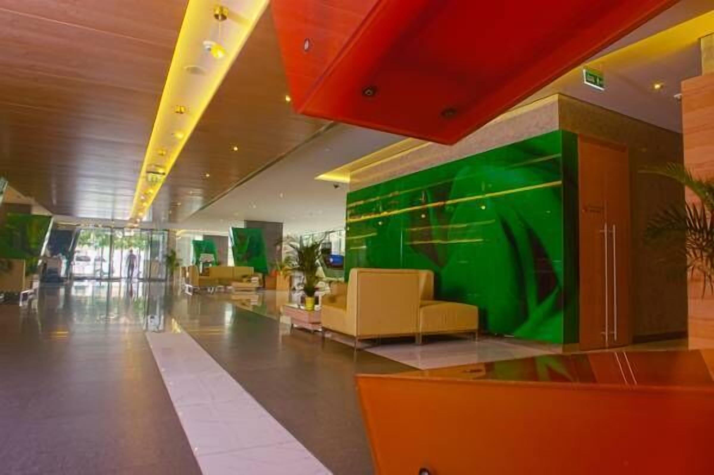 Un lobby espacioso con diseño moderno, que presenta una pared de acento verde, un sofá amarillo y un techo rojo.