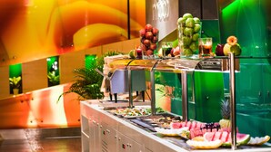 Ein Buffet mit verschiedenen Früchten und Gemüsesorten, darunter Wassermelone, Ananas und Trauben, in einem hell erleuchteten Raum mit grünen und orangefarbenen Akzenten.