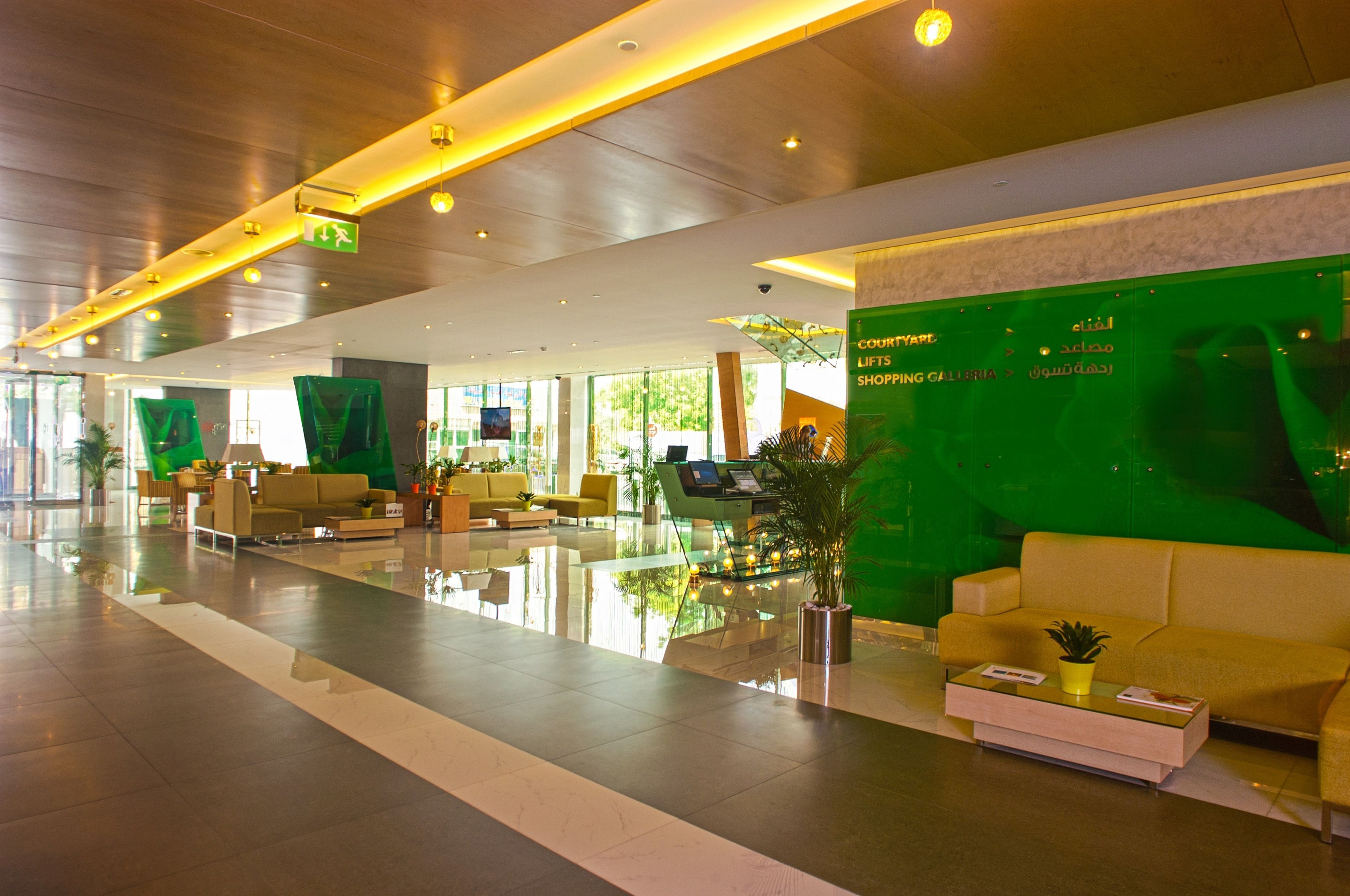 A spacious lobby with a glass coffee table, yellow sofas, and a green wall with a sign.
