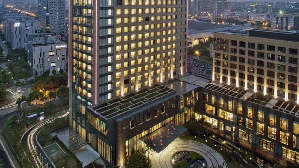 Un hôtel de grande hauteur, doté d’une façade moderne en verre, de nombreux étages et d’un hall d’entrée bien éclairé.