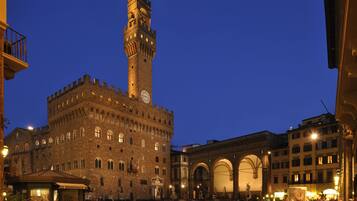 A historic building with a prominent tower and clock, surrounded by a square with people and shops.