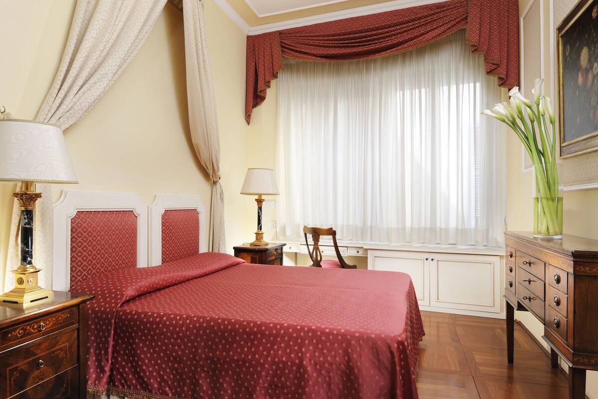 A bedroom with a large bed, two bedside tables, a dresser, a chair, and a window with curtains.