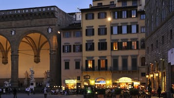 A historic square with a prominent archway and a building with a restaurant sign.