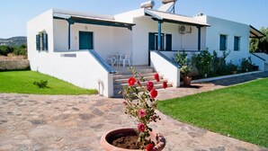 A modern two-story house with a stone-paved entrance, a staircase leading to the main door, and a small garden with a potted plant. - Fotini Apartments (Sitia)