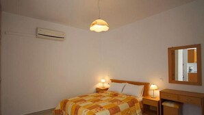 A bedroom with a bed, bedside lamps, a nightstand, a dresser, a mirror, and an air conditioning unit. - Fotini Apartments (Sitia)