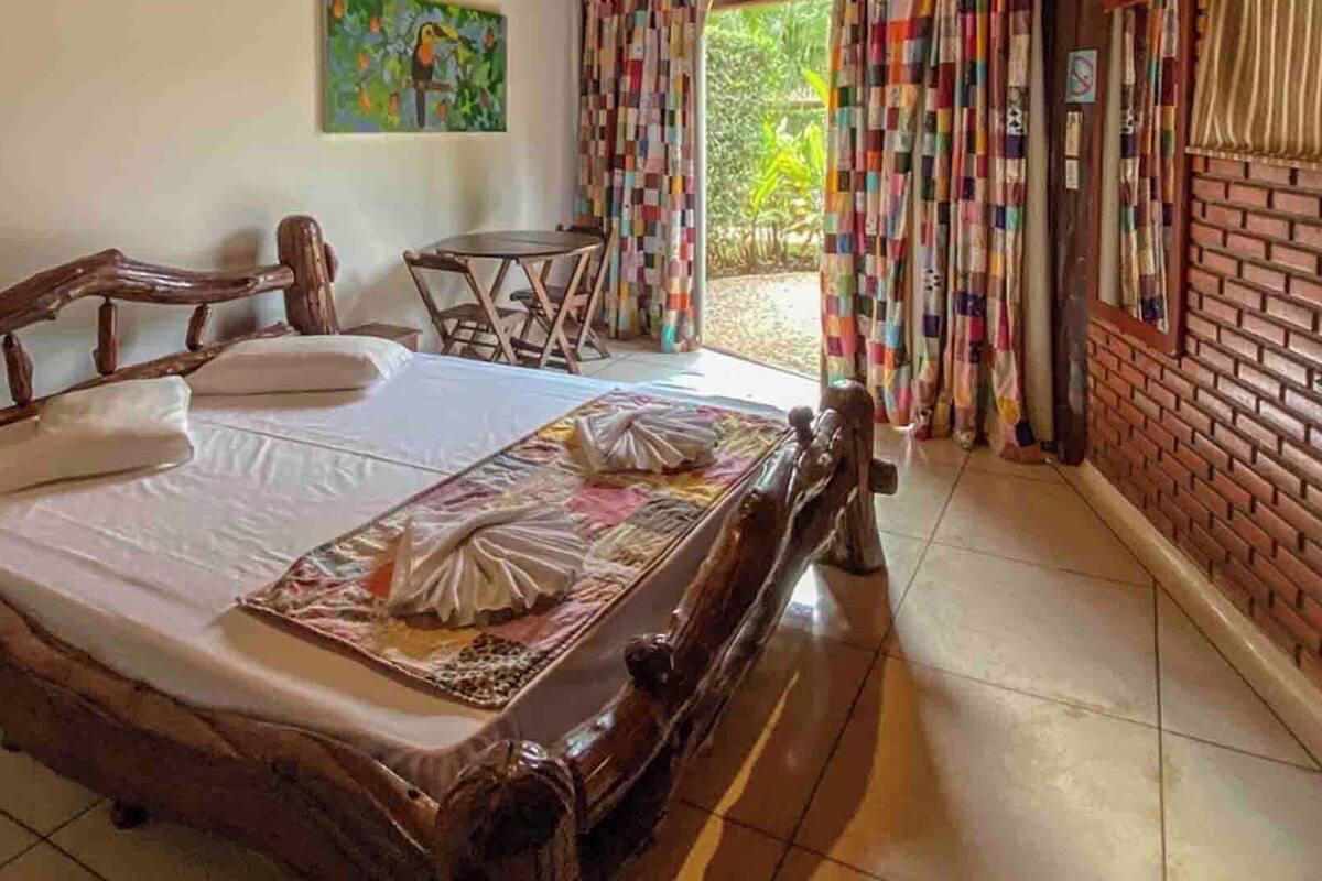 A wooden bed with white linens, a small round table, and colorful curtains.