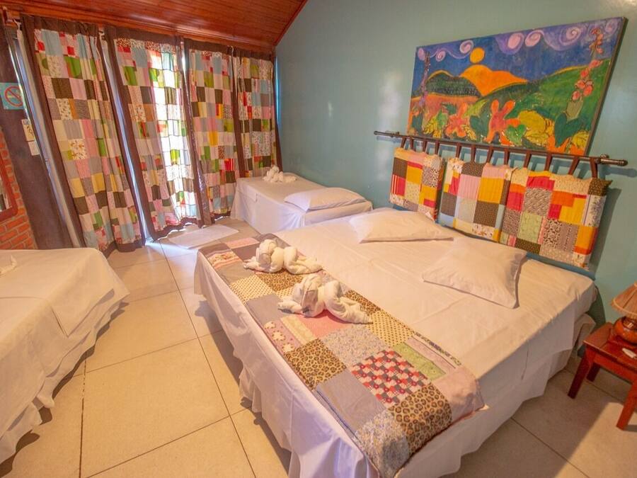A hotel room with two beds, a quilted curtain, a painting, and a lamp.