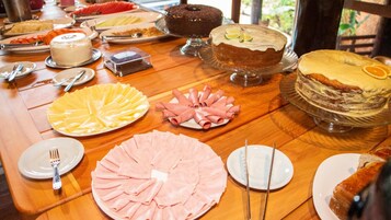 Uma mesa de buffet com diversos pratos, incluindo bolos, um prato de presunto e um prato de queijos.