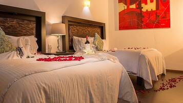 A hotel room with two beds, a nightstand with a bottle and glasses, and a wall with a red abstract painting.