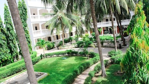 A courtyard with a pathway, palm trees, and a building with balconies. - Sunu Hotel (Serrekunda)