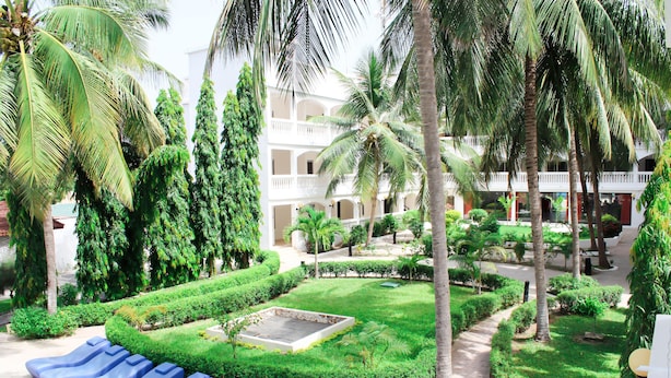 A courtyard with a pool, palm trees, and a building with balconies. - Sunu Hotel (Serrekunda)