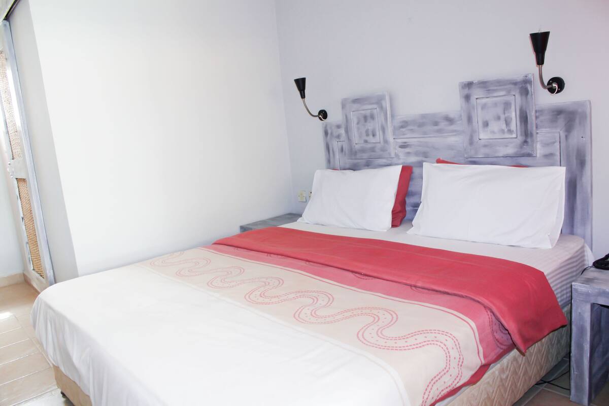 A neatly made bed with white and red bedding, two bedside tables, and a wall-mounted light fixture.