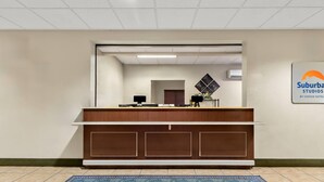 A reception desk with a flat-screen monitor, a telephone, and a small plant. There is a blue patterned rug on the floor. - Suburban Studios Morgantown (Morgantown)