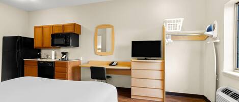 Habitación de hotel pequeña y funcional con cama, kitchenette, escritorio y televisor.