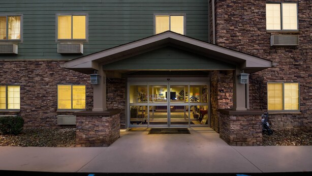 A building with a stone facade, multiple windows, and a central entrance with a door and a small overhang. - Suburban Studios Morgantown (Morgantown)