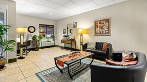 A living room with a black leather sofa, a coffee table, a dining table, and a potted plant. - Suburban Studios Morgantown (Morgantown)
