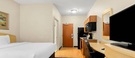 A hotel room with a bed, desk, chair, television, and a small kitchenette.
