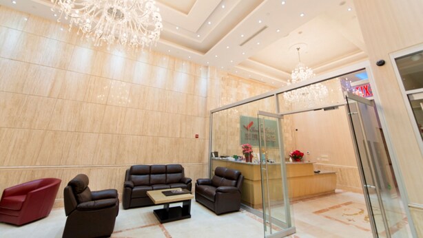 A modern lobby with a reception desk, leather sofas, a glass partition, and a chandelier.