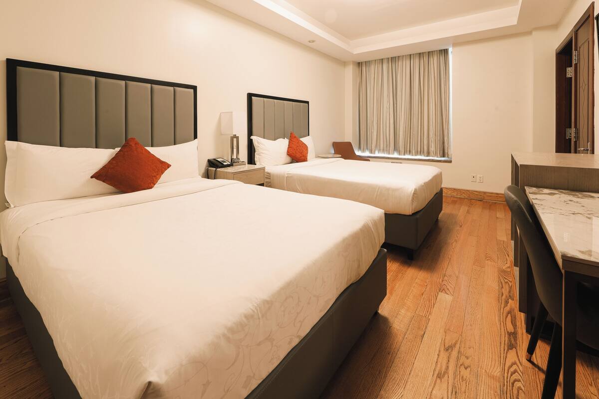 A hotel room with two beds, a desk, and a window with curtains.