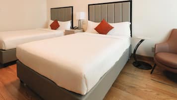 A hotel room with two beds, a small table, a chair, and a nightstand with a lamp.