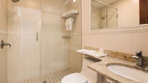 A modern bathroom with a glass-enclosed shower, a white toilet, a granite countertop sink, and a mirror above the sink.