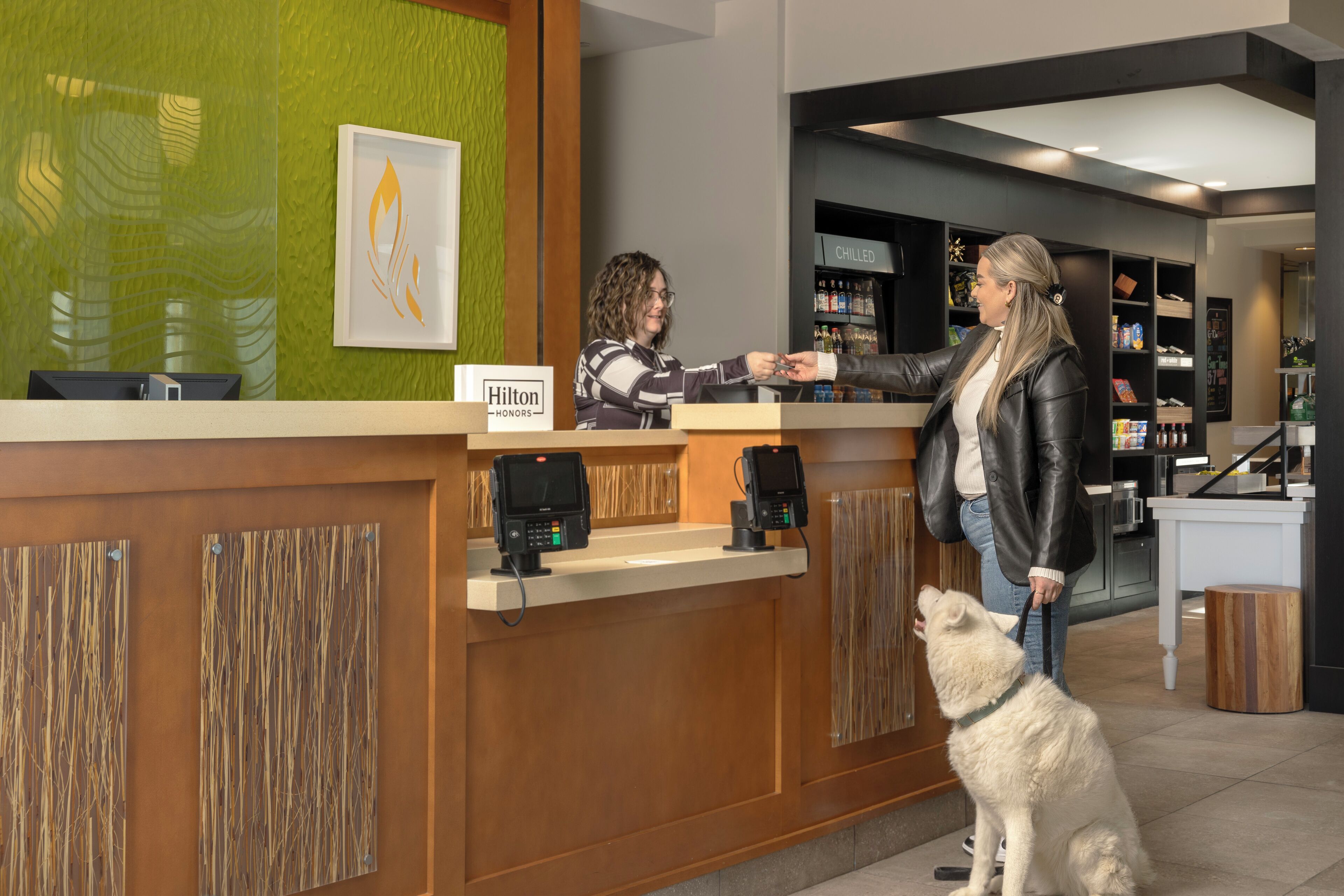 A hotel reception desk with a green wall, a framed artwork, and a sign indicating 'Hilton Honors'.