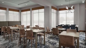 A hotel dining area with multiple tables and chairs, large windows, and a marble-patterned carpet.