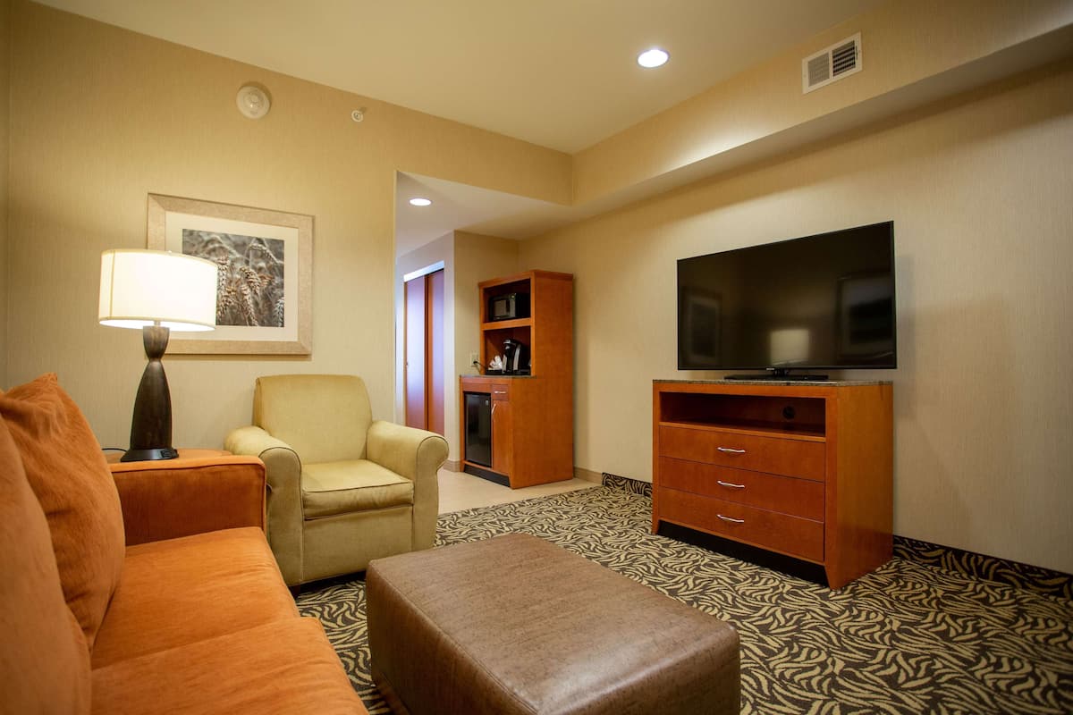 A hotel room with a sofa, armchair, ottoman, television, and a cabinet.
