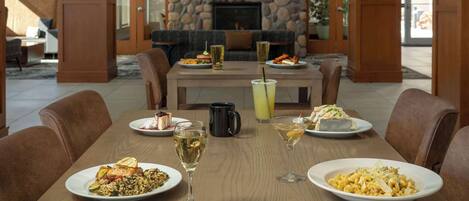 Una mesa de comedor dispuesta con diferentes platos, bebidas y una chimenea al fondo.