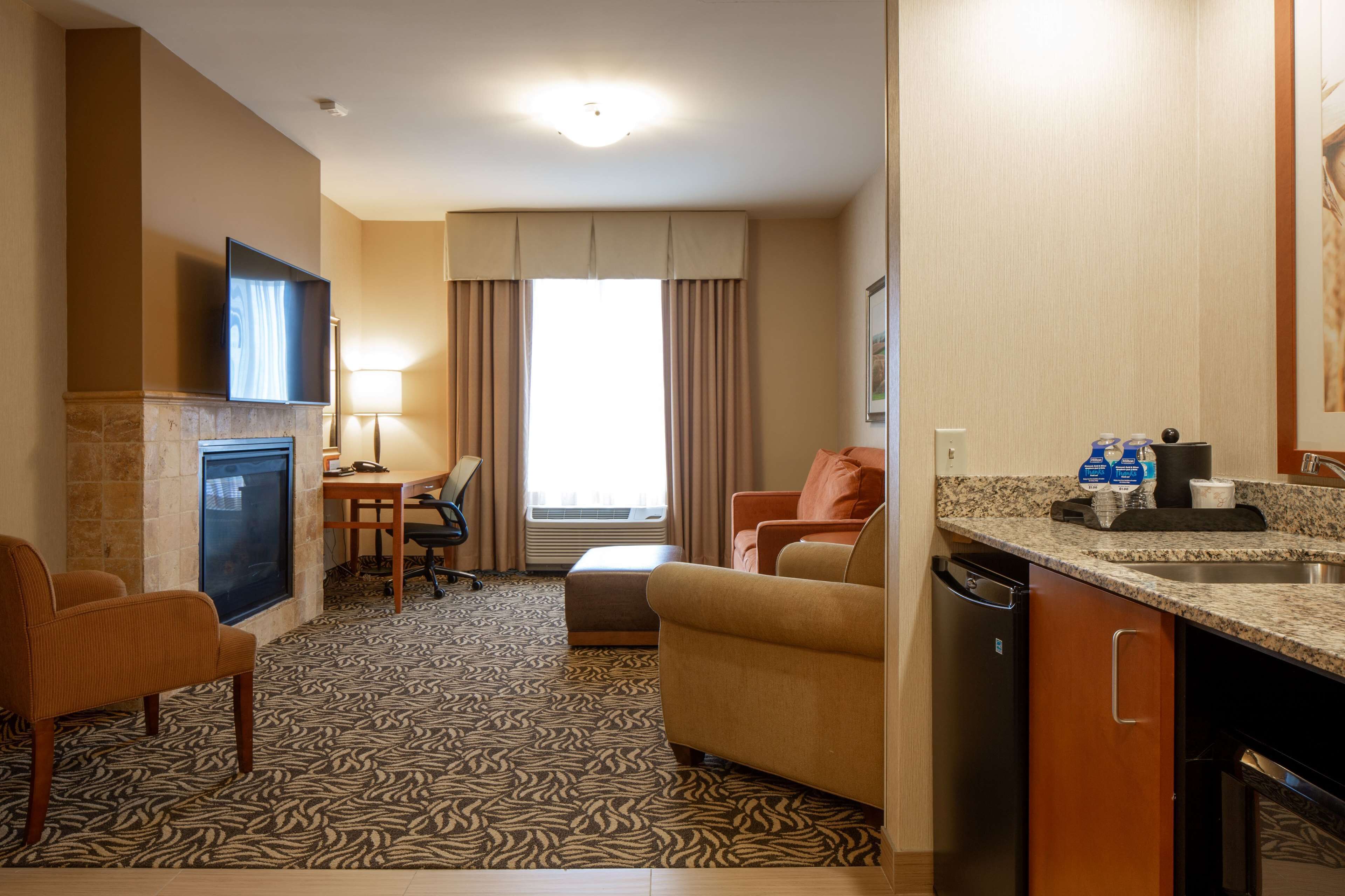 Une chambre d’hôtel dotée d’un téléviseur à écran plat fixé au mur, d’un coin repas avec une table et des chaises, d’un canapé, d’un coin cuisine avec un évier et un plan de travail, et d’un tapis à motifs.