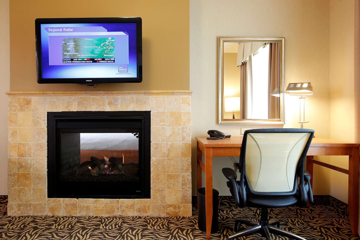 A hotel room with a television displaying a regional radar, a fireplace, a desk with a chair, and a mirror.