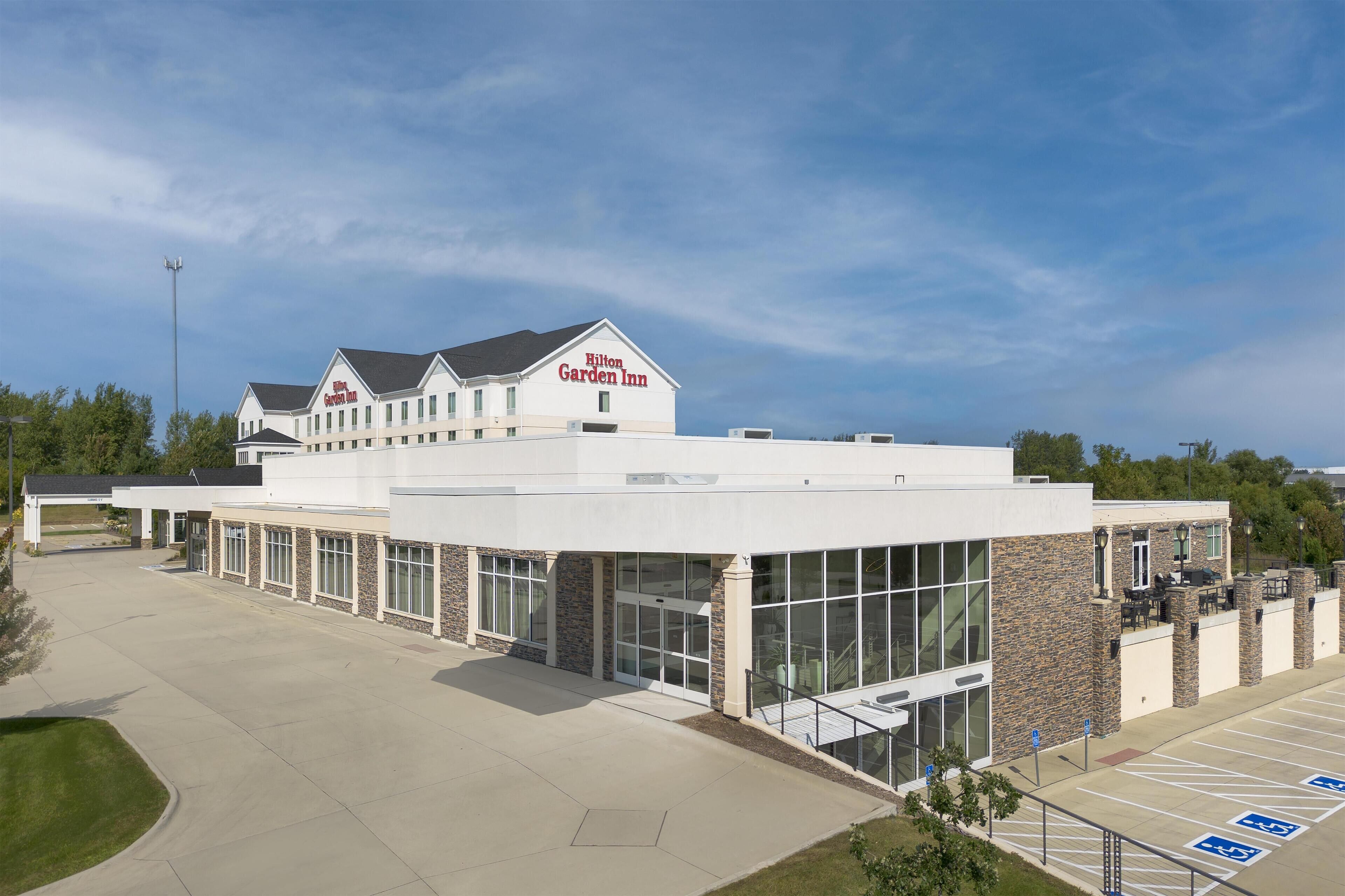A modern hotel with a large glass facade, a prominent Hilton Garden Inn sign, and a spacious parking area with handicap-accessible spots.