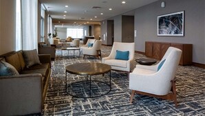 A spacious lobby with a patterned carpet, a variety of seating options including sofas and armchairs, and a large window providing natural light. - Hilton Garden Inn Cedar Falls (Cedar Falls)