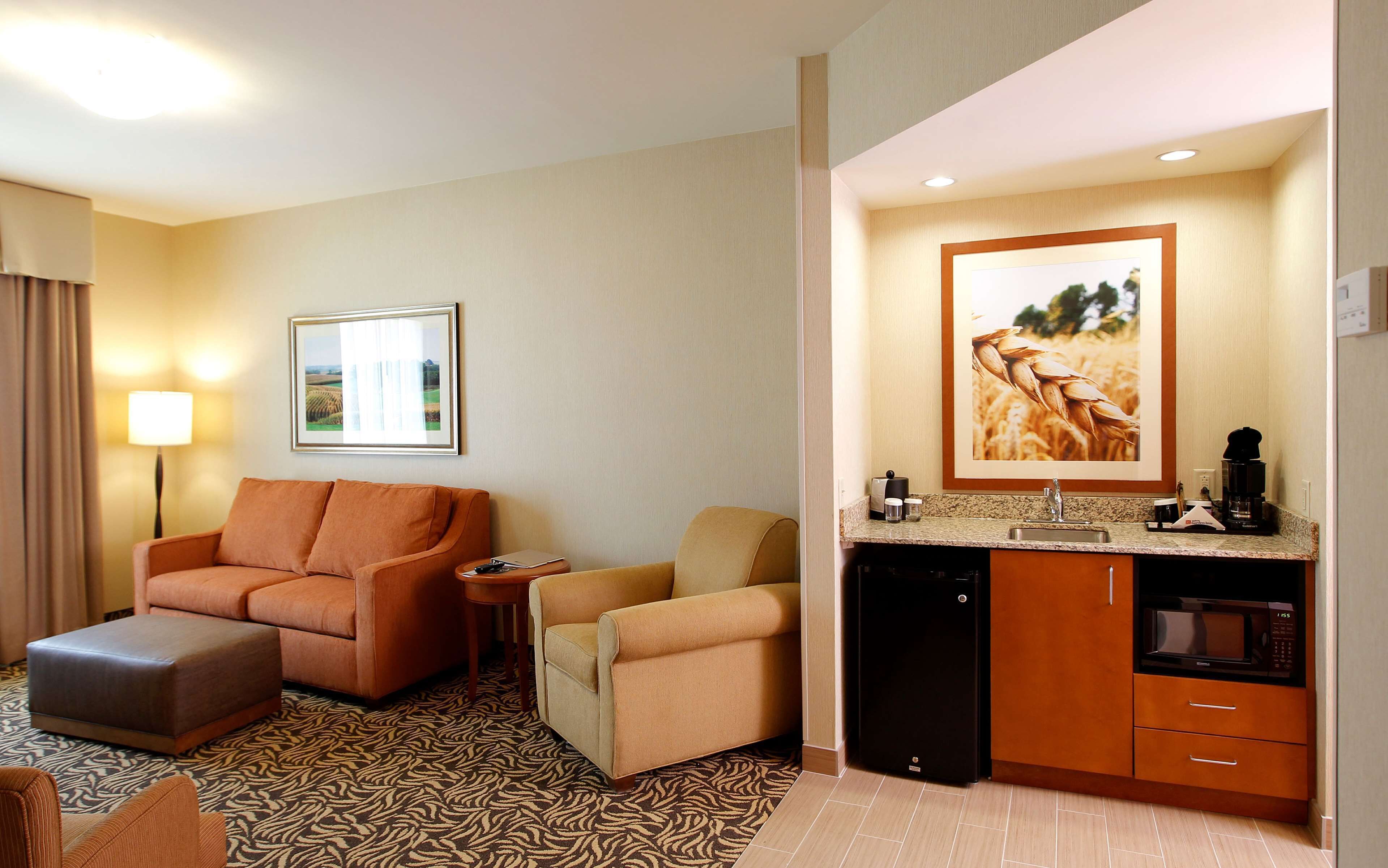 A hotel room with a sofa, ottoman, a small table, a desk, a microwave, and a coffee maker.