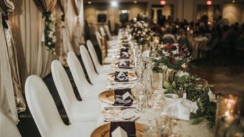 A long banquet table set with white chairs, glassware, and floral centerpieces.